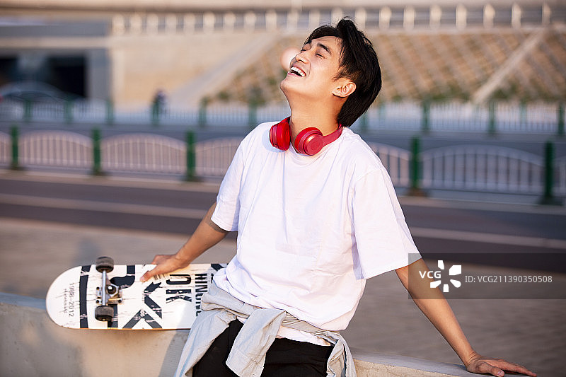 滑完滑板靠着栏杆休息的年轻男子图片素材