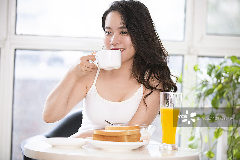 漂亮的年轻女子在家吃早餐喝咖啡图片素材