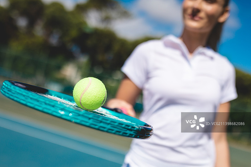 阳光灿烂的日子里，年轻的白人女性选手拿着球拍站在网球场上微笑图片素材