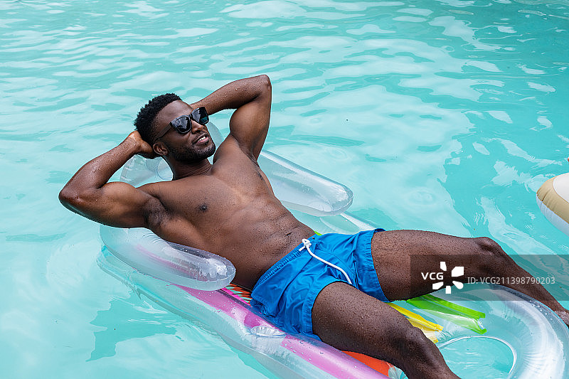 赤膊的非洲裔美国年轻人，穿着短裤，在游泳池的充气环上放松图片素材