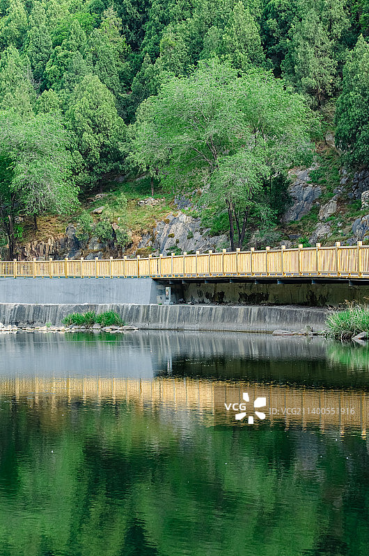 中国自然风光拍摄主题，山东省泰安市岱岳区彩石溪风景区，绿色的山区树林和河道里的石头，路边的黄色栈道台图片素材