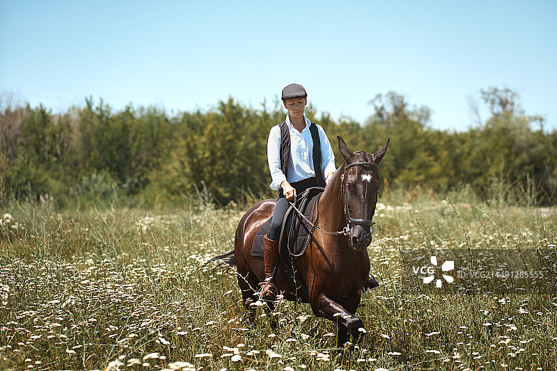 宁静的女人骑着她的棕色马，在非城市的环境中享受。她戴着平顶帽图片素材