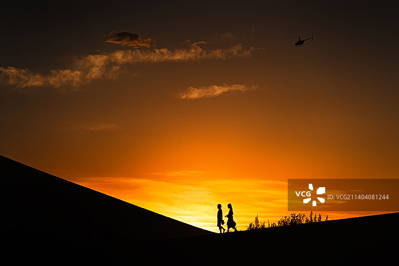夕阳下，一堆恋人行走在沙丘上图片素材