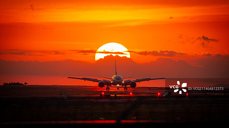 哥斯达黎加阿拉胡埃拉省，一架飞机在太阳附近的剪影，太阳在红云中图片素材