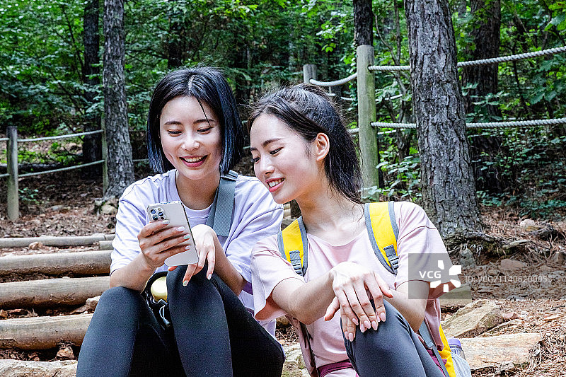 韩国年轻女性徒步旅行，坐着看智能手机图片素材