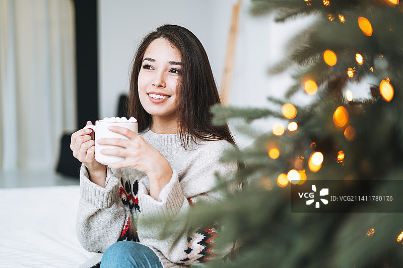 俄罗斯斯维尔德洛夫斯克州叶卡捷琳堡，一名年轻女子穿着舒适的毛衣，在房间里放着一杯有棉花糖的可可，家里有圣诞树图片素材