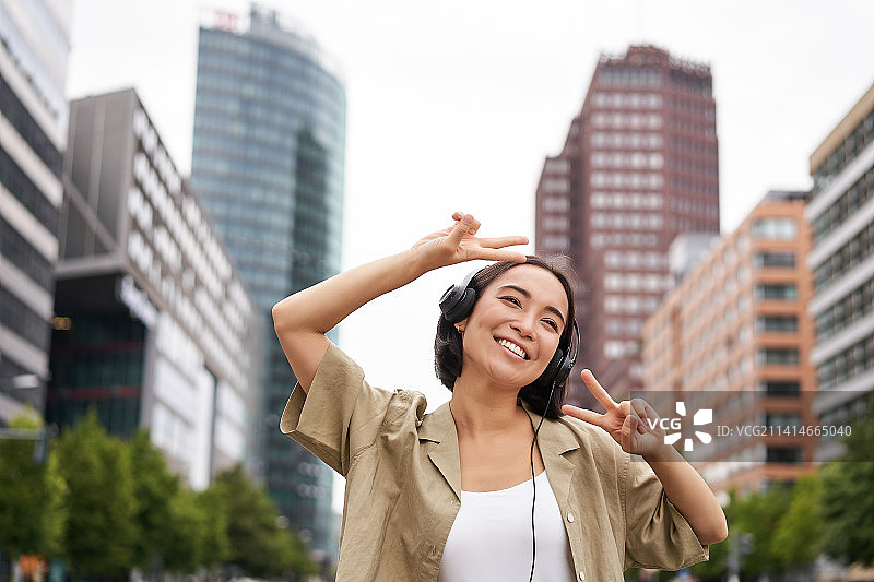 快乐的亚洲女人戴着耳机，听着音乐，在街上跳舞图片素材