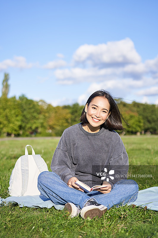 垂直拍摄可爱的少女坐在公园的草地上背着背包图片素材