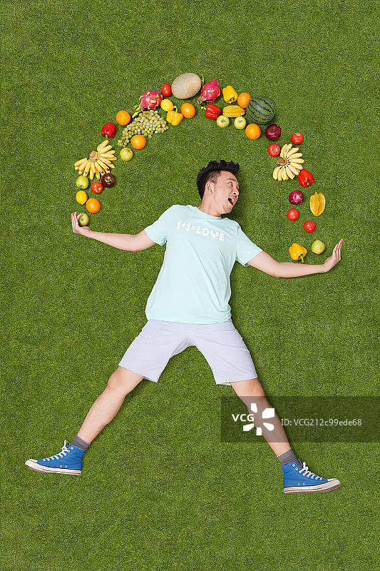 年轻男子躺在草地上手托着水果图片素材