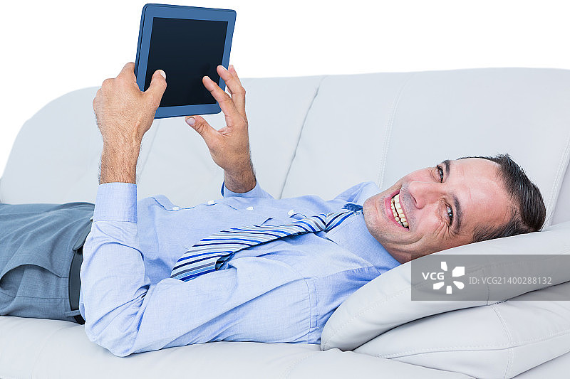 悠闲的商人坐在沙发上，背靠一堵白墙，拿着平板电脑图片素材