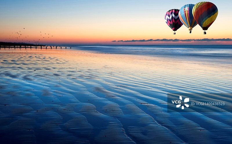 美丽的低视角沿着海滩在低潮出海与生气勃勃的日出天空与热气球在海上图片素材