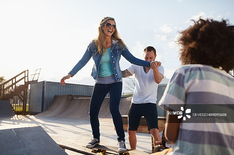 男友帮助女友在阳光滑板公园滑板图片素材