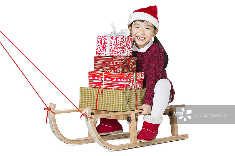 小女孩拿着圣诞礼物坐在雪橇上图片素材
