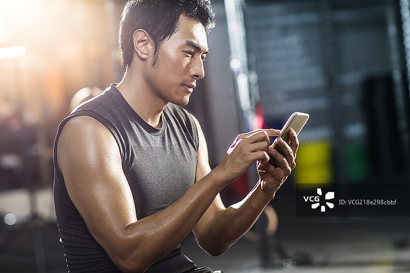 年轻男子坐在健身房使用手机图片素材