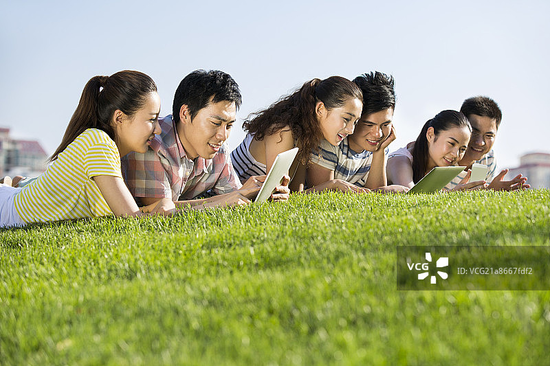 情侣们在草地上玩平板电脑和手机图片素材