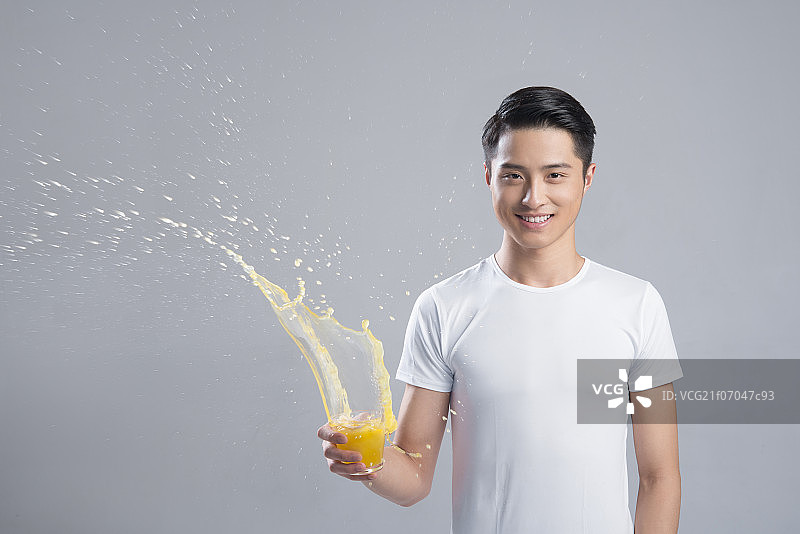 Young man with splashing orange juice图片素材