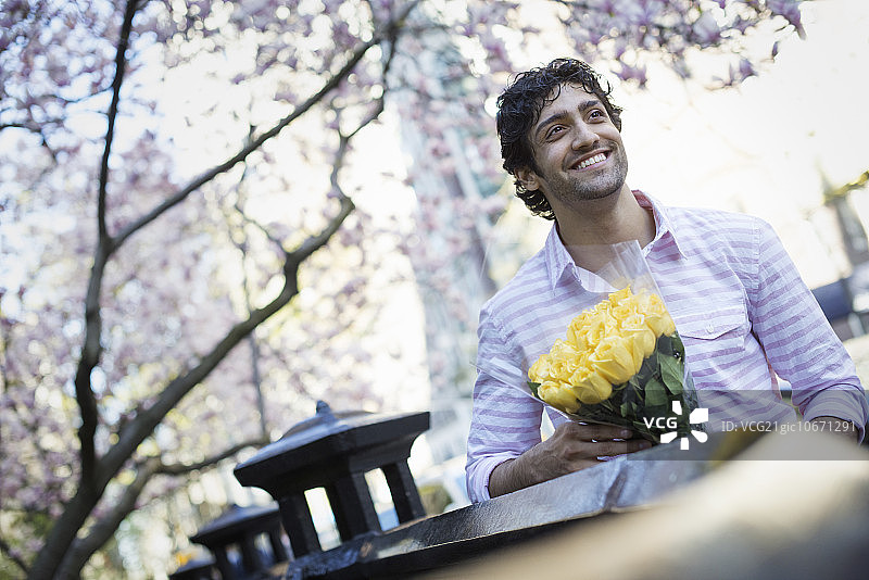 城市生活。一个年轻人在春天的公园里，手里拿着一束黄玫瑰。图片素材