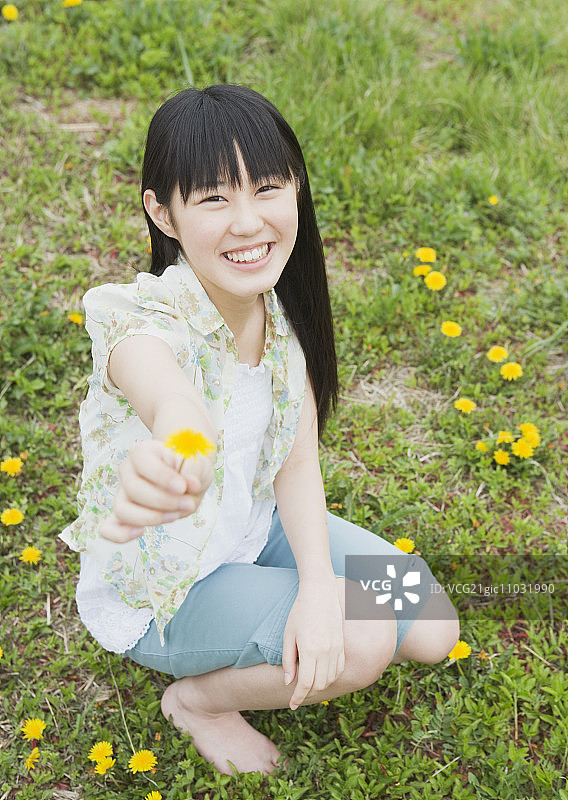 女孩，坐在田野里，微笑着摘了一朵花图片素材