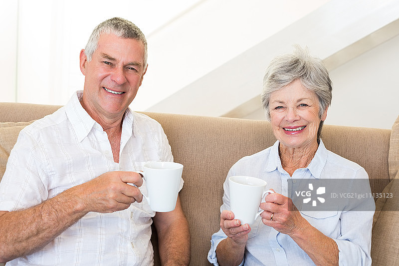 老夫妇坐在沙发上喝咖啡，在客厅对着镜头微笑图片素材