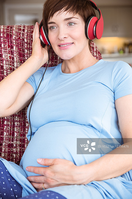 一名孕妇在起居室里戴着耳机图片素材