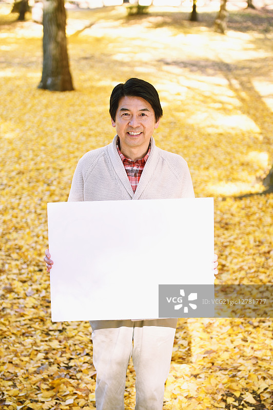 秋天，在城市公园里，一个日本老人拿着白板图片素材
