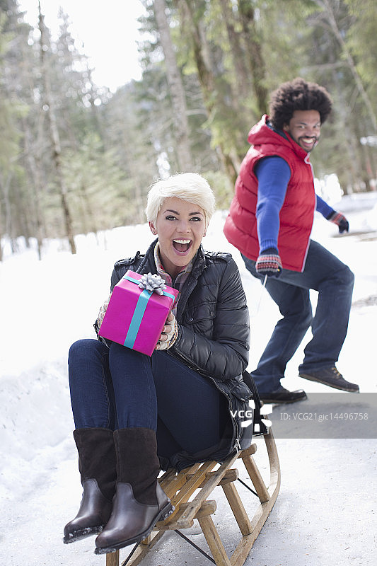 一个男人在雪地里用雪橇拉着一个女人带着礼物图片素材