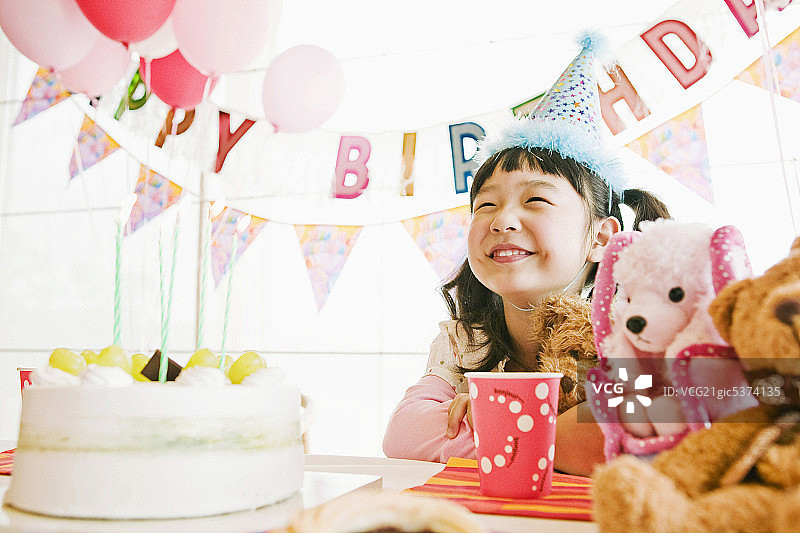 女孩坐在桌前，面带微笑，拿着插着蜡烛的生日蛋糕图片素材