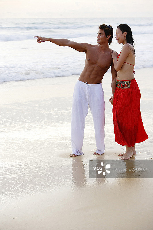 一对情侣站在沙滩上，手牵着手，男人指着图片素材