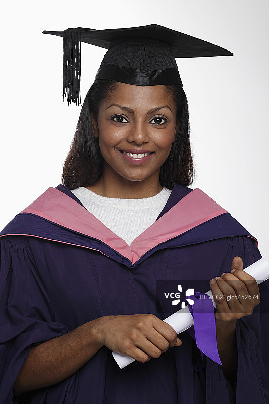 年轻女子戴着毕业帽和毕业袍，拿着毕业证书图片素材