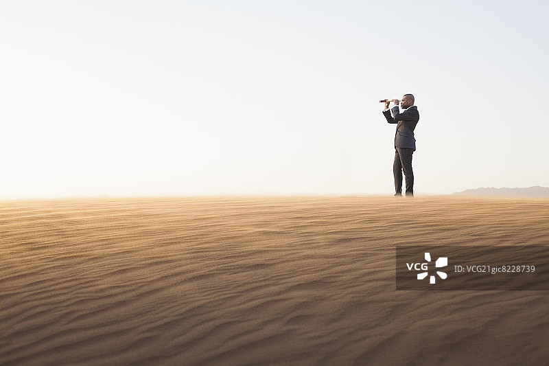 一个年轻的商人正在用望远镜观察沙漠中的景象图片素材