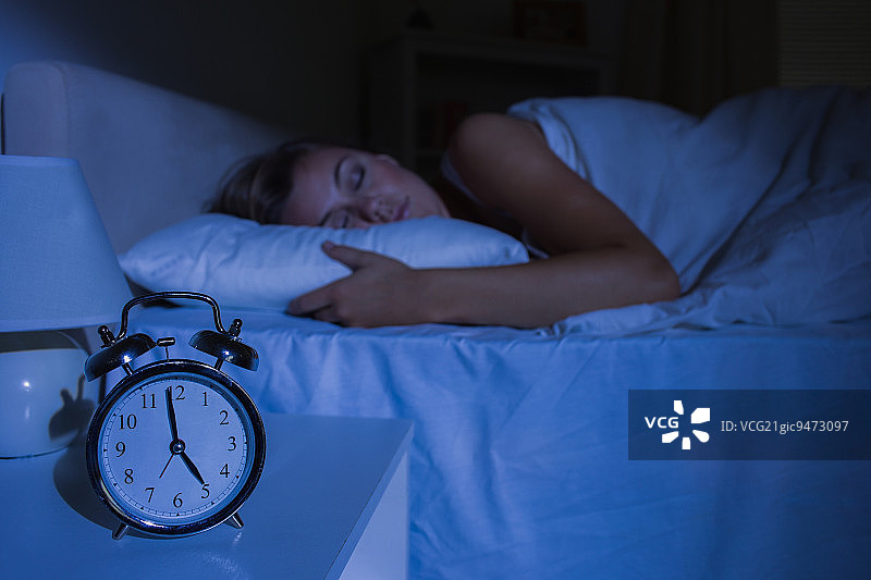 晚上把注意力集中在卧室里睡觉的女人面前的闹钟上图片素材