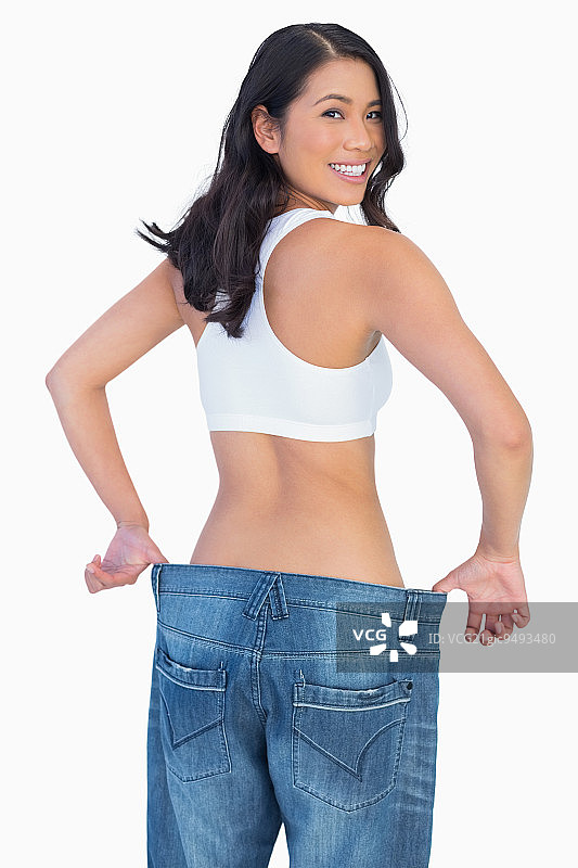 一个女人拿着她太大的牛仔裤对着白色背景的相机微笑图片素材