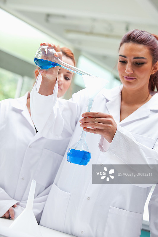 在实验室里，科学家们微笑着将液体倒入烧瓶图片素材
