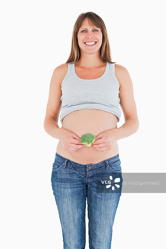 美丽的孕妇拿着一个花椰菜，而站在一个白色的背景图片素材