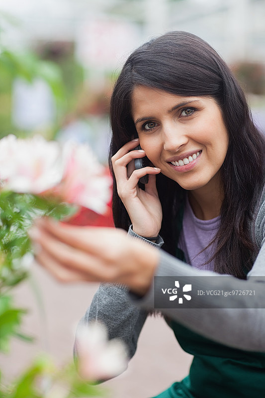 微笑的花商，触摸鲜花和打电话在花园中心图片素材