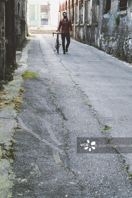 西班牙毕尔巴鄂，一个骑着赛车的人走在旧工业区的一条小巷里图片素材
