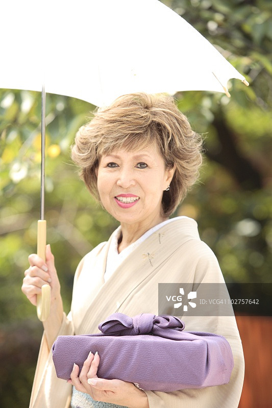 日本京都市，京都县，成年妇女在和服撑伞和礼物的肖像图片素材