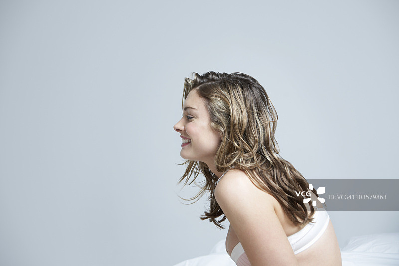 年轻女子在内衣的侧面，在床上微笑，特写图片素材