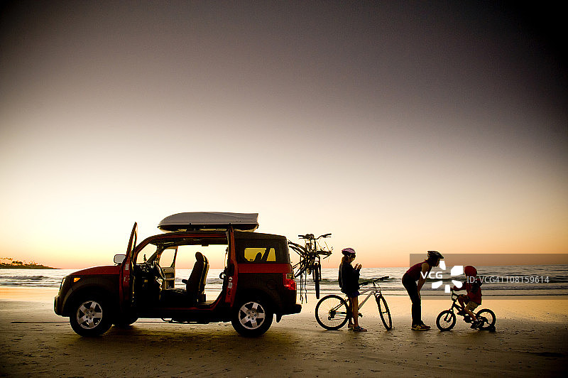家人在海滩上骑自行车和汽车，日落图片素材