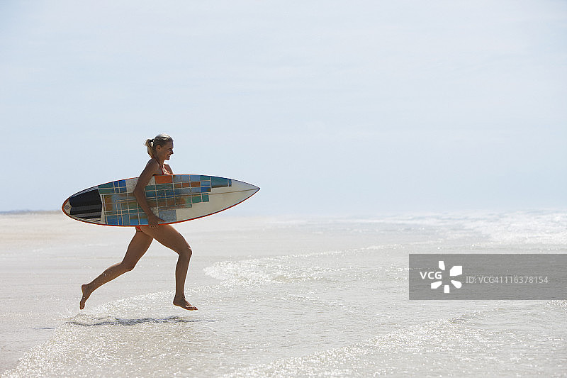 带着冲浪板在海滩上跑步的女人图片素材