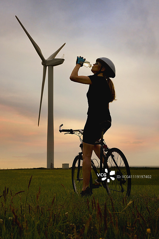 日落时，女自行车手靠近风力涡轮机图片素材