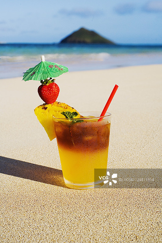一杯配着菠萝和草莓的迈泰鸡尾酒，坐在沙滩上的沙滩上。图片素材