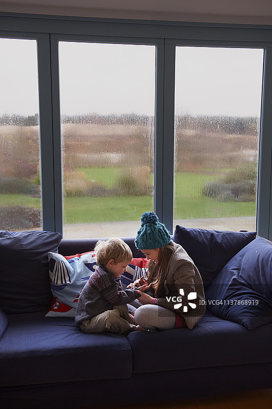 兄弟姐妹坐在下雨的窗户前的沙发上图片素材