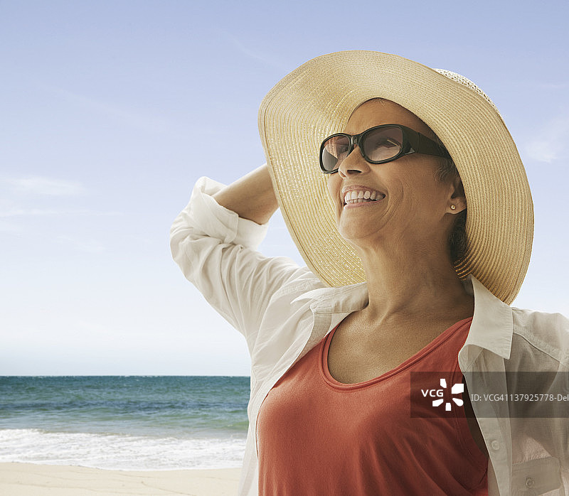 一个女人拿着帽子站在海滩上挡风图片素材