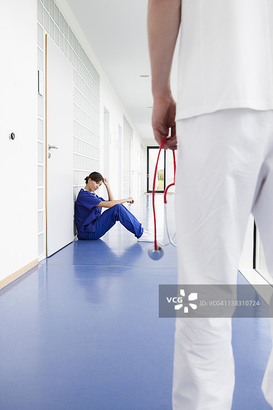 德国，巴伐利亚州，Diessen am Ammersee，年轻的女医生坐在走廊里，男医生站在前景图片素材
