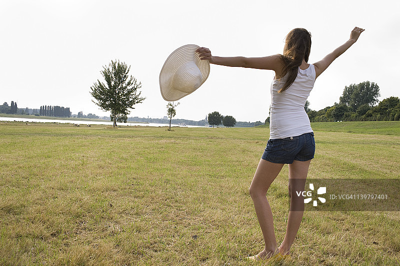 年轻女子站在草地上，双臂张开图片素材