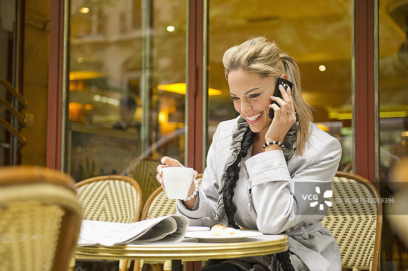 西班牙妇女喝咖啡和使用手机在户外咖啡馆图片素材