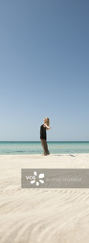 女人站在沙滩上，胳膊伸着，侧视图片素材