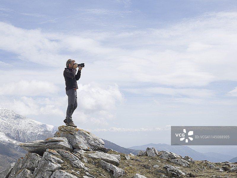 一个人站在岩石的顶端，用单反相机拍照图片素材