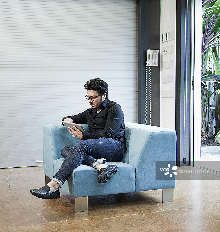 西班牙裔男子坐在椅子上使用数字平板电脑图片素材